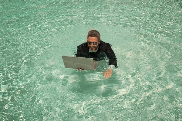 smiling businessman has freelance business online. businessman has freelance business in swimming pool. businessman has freelance business with laptop. photo of businessman has freelance business