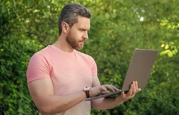 concentrated freelancer man outdoor. freelancer man work online. photo of freelancer man freelancing. freelancer man with laptop.