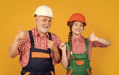 Mutlu çocuk ve büyükbaba sarı arka planda kalın şapkalı inşaatçı. başparmak yukarı.
