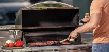 Adam yaz gününde nefis ızgara yapıyor. Adam arka bahçede ızgara yemek hazırlıyor. Barbekü partisinde ızgara yapan adam. Lezzetli ızgara kreasyonları.