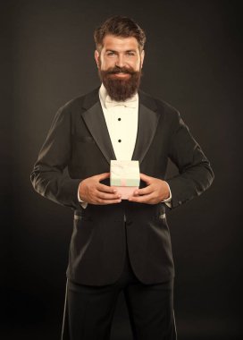 Siyah arka planda smokinli, papyon takan, hediye kutusuyla gülümseyen adam. Boks günü.