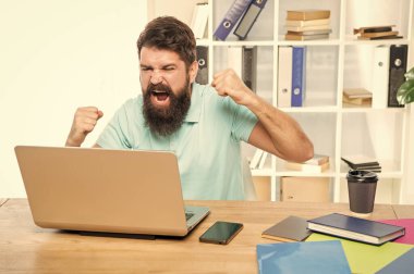 Heyecanlı adam dizüstü bilgisayarda bağırmaktan mutlu. Ofis masasında zafer jesti yapıyor..