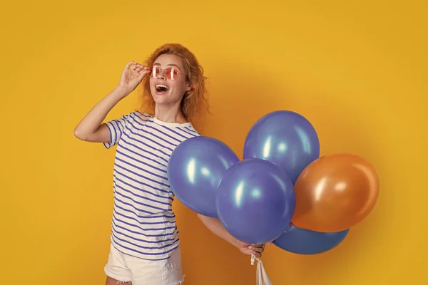 party girl with balloon in sunglasses. caucasian girl hold party balloons in studio. girl with balloon for party isolated on yellow background.