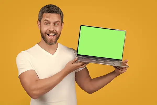 amazed man showing laptop app in studio. man showing app on laptop. man showing app on screen with copy space. man showing app isolated on yellow background.