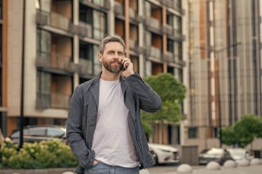 Yetişkin adamın dışarıda akıllı telefon görüşmesi var. Sokakta akıllı telefon görüşmesi yapan bir adam. Adam dışarıdaki akıllı telefondan arıyor. Adamın fotoğrafı. Akıllı telefondan ara ve konuş..