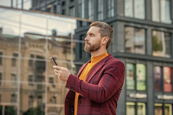 stylish man messaging on smartphone outdoor. man messaging on smartphone in the street. man messaging on smartphone outside. photo of man messaging on smartphone in jacket.