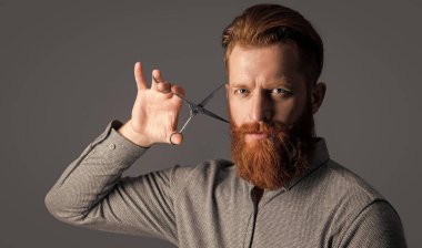 Kuaför stüdyosunda erkek portresi. Adam saç kesimi için kuaför makası tutuyor. Erkek saç kesimi kavramı. Erkek kuaför saç kesimini gri renkte yapar. Kestirmek için makaslı kuaför..