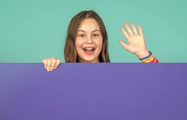 Boş mavi kağıdın arkasında reklam için fotokopi alanı olan mutlu bir çocuk. Merhaba işareti..