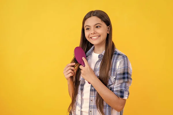 stock image cheerful teen girl brushing hair with hairbrush. Beautiful teen girl with hairbrush. teen girl using hairbrush to style hair isolated on yellow. teen girl holding hairbrush while brushing her hair.