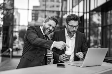 Mutlu tüccarlar online olarak dışarıda serbest çalışıyorlar. Ticari tüccarlar dizüstü bilgisayarla serbest çalışıyorlar. Tüccarların internetten serbest iş yaparken çekilmiş bir fotoğrafı. İki tüccar online olarak serbest çalışıyor..