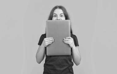 Sarı arka planda dizüstü bilgisayarın arkasında mutlu bir kız.