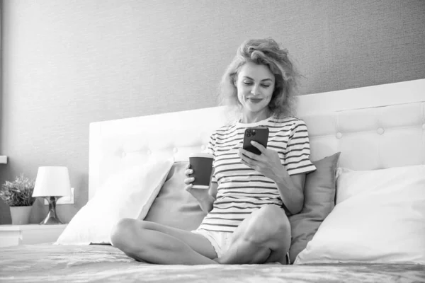 positive woman with coffee surfing internet on phone. woman surfing internet at home with phone. internet surfing at home of woman.