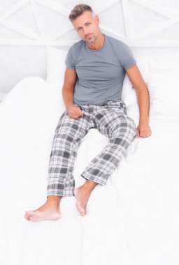 Man enjoying rest in bed. Man resting in bed. Man having rest in morning. Man in pajamas relaxing on white bedclothes. Morning rest.