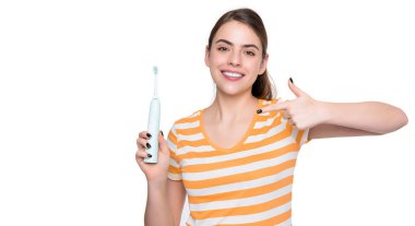 Mutlu genç kadın, beyaz arka planda izole edilmiş elektrikli diş fırçasını işaret ediyor..