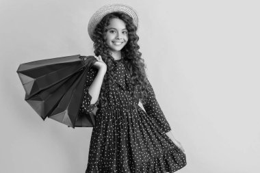 positive child with curly hair hold shopping bags on yellow background.