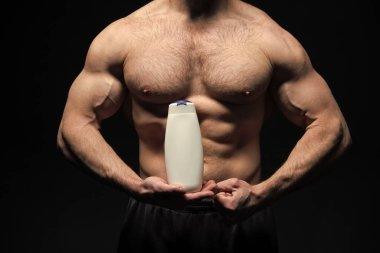 Erkek kozmetik ürünleri olan kaslı adam siyah arka planda izole edilmiş. Stüdyoda kozmetik ürünleri satan kaslı bir adam. Güçlü kaslı adam kozmetik ürünlerini elinde tutuyor. Erkek makyaj şampuanıyla kaslı bir adamın fotoğrafı..