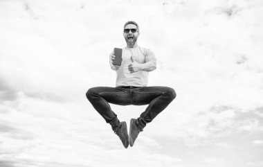 man jumping and presenting smartphone on sky background. thumb up.