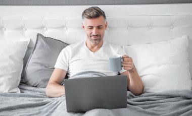 Mutlu olgun bir adam laptopta çalışıyor ve kahve içiyor..