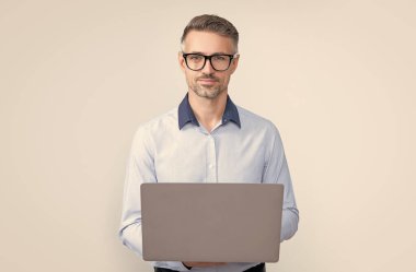 Gri arkaplanda bilgisayar üzerinde çalışan gözlüklü olgun bir yönetici.