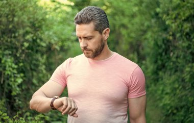 Yakışıklı, tıraşsız adam kol saatini kontrol ediyor. Doğal arka plan, dakiklik..