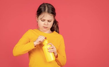 Çocuk pembe arka planda su şişesini fotokopi alanı ile tutuyor.