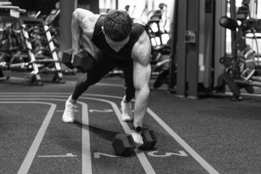 Spor salonunda dambıllarla tahta döşeyen bir sporcu. Spor salonundaki atletik adam, halterli döşeme sırası yapıyor. Fitness egzersizi. Form ve çekirdek gücü geliştiriliyor..