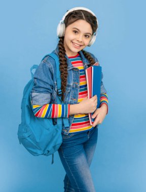 Happy teenager listening to audiobook in headphones. Happy teenage girl listening to audio course blue background. Listening skills. School education.