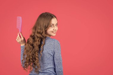 Kıvırcık saçlı mutlu genç kız pembe arka planda tarak tutuyor..