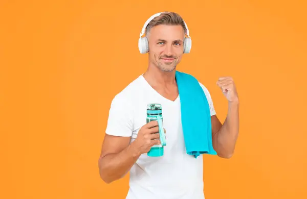 stock image successful guy with towel and bottle after training. guy hold bottle for healthy lifestyle. guy with sport bottle for healthy lifestyle isolated on yellow. guy holding bottle to keep sport lifestyle.