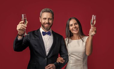 Şampanyayla kutlama yapan zarif bir çift. Kadehler. Resmi smokinli çift kırmızıda izole edilmiş bir şekilde tezahürat yapıyor. Smokinli çift resmi olarak tezahürat yapıyor. Resmi smokinli çiftin tezahüratlarının stüdyo çekimi..