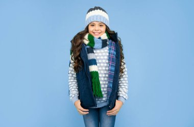 Mavi arka plandaki duygusal genç kız. Kalın giysiler giyen çocuk. Olumlu duygularını ifade et. Kış modası. Şapkalı ve atkılı mutlu çocuk..