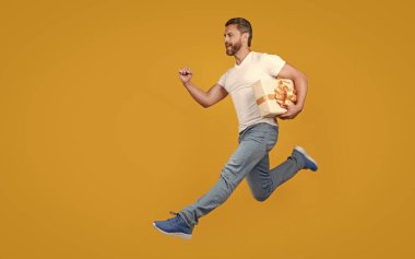 Aktif kurye, hediye kutusuyla havada sarı arka planda koşuyor. Hızlı kurye teslimatı. Kurye servisi, boşluğu kopyala.