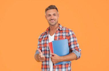 Okul kitaplarını sarı arka planda tutan gündelik parmakla işaret eden mutlu adam, öğrenci..