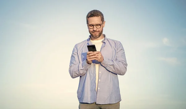 man in glasses chat on smartphone with message. man chatting on phone messaging. smartphone communication. man chat on sky background.