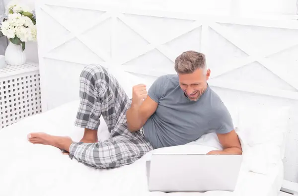 successful man freelancer at home. man freelancer at home in bed. man freelancer at home in bedroom. photo of man freelancer at home with laptop.