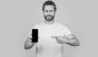 Adam arka planda akıllı telefon uygulaması gösteriyor, işaret ediyor. Stüdyoda akıllı telefon uygulaması gösteriyor. Akıllı telefon uygulaması gösteren bir adamın fotoğrafı. Akıllı telefon uygulaması gösteren adam sarıda izole edildi.