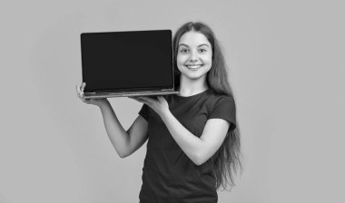 Sarı arka planda dizüstü bilgisayarı olan neşeli bir çocuk..