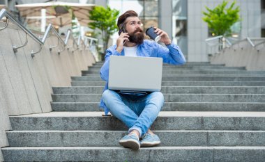 Cep telefonuyla konuşan sakallı adam kahve içiyor. Dışarıdaki merdivenlerde dinlenen bir adam mobil arama yapıyor. Cep telefonundan arıyorlar. Mobil iletişim. Telefon görüşmesi.