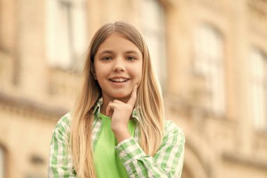 Portrait of happy teen girl smiling with finger on cheek blurry outdoors.