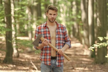 Unshaven axeman man in lumberjack style standing with axe forest background.