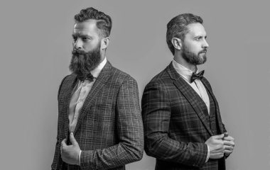 Formalite giymiş yakışıklı smokinli adamlar gri arka planda izole edilmiş. Smokinli iki adam resmi kıyafet giyiyor. Stüdyoda resmi kıyafet giyen adamlar. Resmi takım elbiseli şık erkekler..