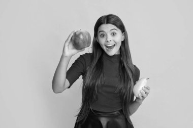 Gülümseyen şaşkın çocuk sarı arka planda elma ve armut tutuyor..