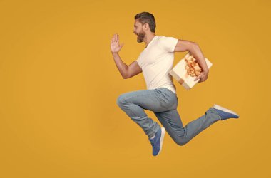 Active man running to deliver present box. Delivery boy in midair yellow studio background. Express delivery service. Fast delivery, copy space.