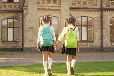 back view of two children with school backpack walking together outdoor.