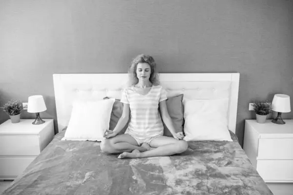 Tranquil woman meditating on bed, meditation. Meditative girl doing mudra gesture relaxing in lotus position. Meditation and deep relaxation. Meditation at home.