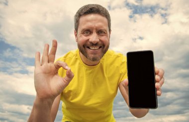 cheerful man presenting screen of smartphone with copy space.