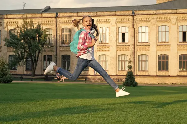 Happy teenage girl jumping in school yard outdoors, back-to-school.