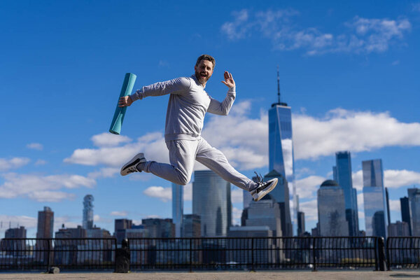 Man jumping with energy. Sport lifestyle. Sportsman running with fitness mat. Sport man training outdoor in New York. Healthy lifestyle with daily fitness. Fitness and sport. Fitness routine.