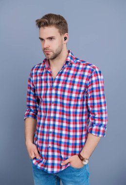 Aleti olan bir milenyum adamı. Kablosuz kulaklıklı bir adam. Adam gri üzerinde kulaklık kullanıyor. Modern kablosuz kulaklıklar. Elsiz kulaklık. Kulaklık cihazı aksesuarı. Kablosuz kulaklık cihazı. Kulaklık Özellikleri.