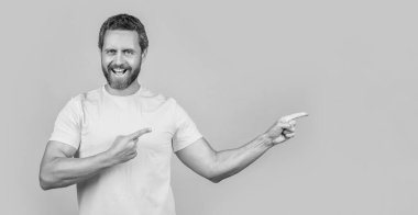 Stüdyodaki reklam teklifini gösteren mutlu adam. Reklam teklifini işaret eden adamın fotoğrafı. Reklam teklifine işaret eden adam sarı üzerine izole edilmiş. Adam reklam teklifini işaret ediyor.